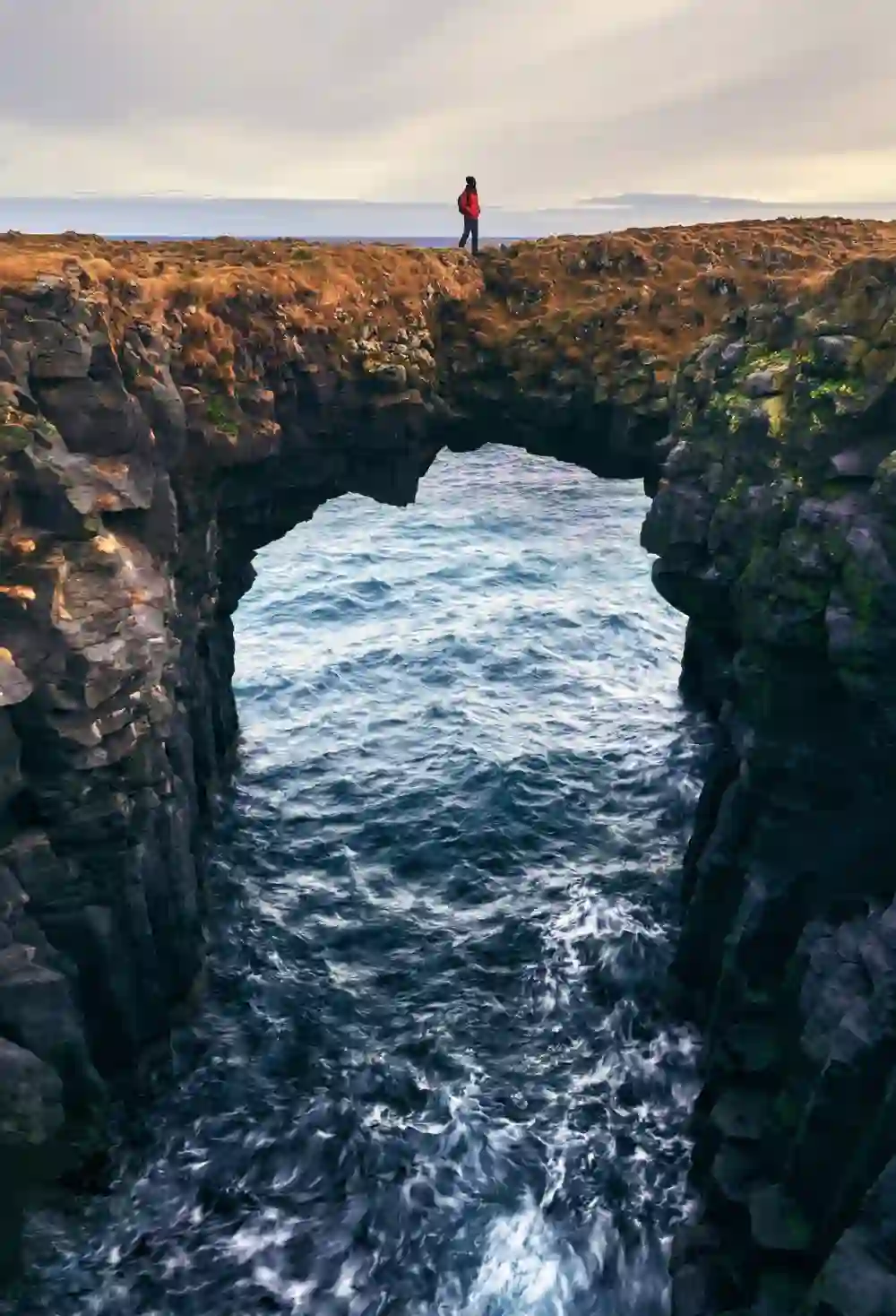 Excursionista junto a un arco de lava en el sendero costero entre Arnarstapi y Hellnar