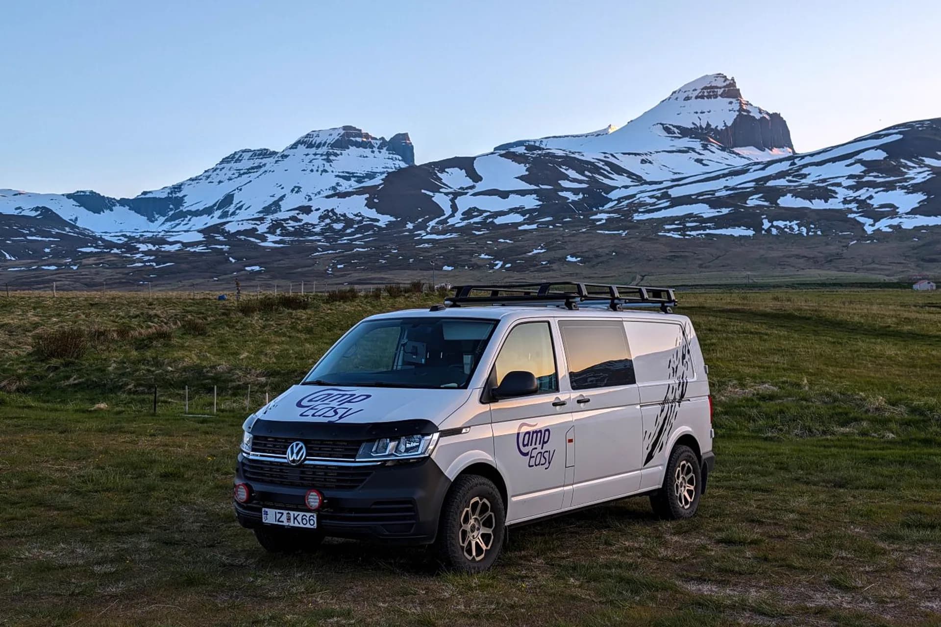 Camper 4x4 de CampEasy aparcada en un prado con montañas nevadas de los fiordos del este de Islandia al fondo