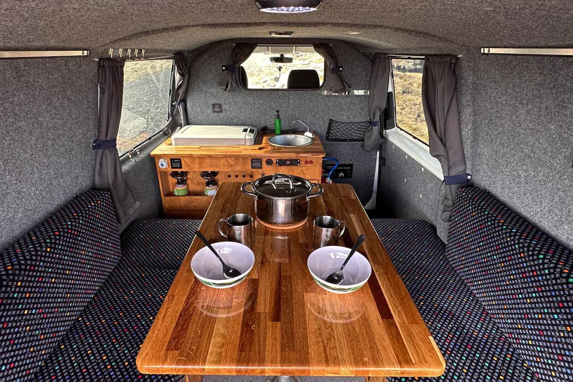 Interior de una camper de CampEasy en Islandia, con mesa de madera, menaje de cocina y vistas a través de las ventanas