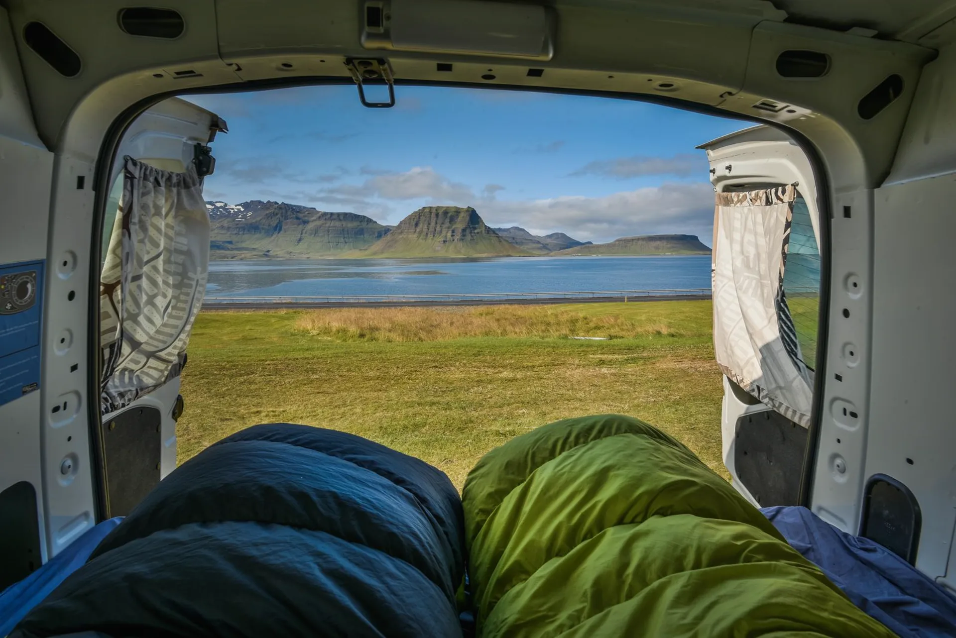 Vista desde el interior de una camper hacia un fiordo de Islandia, con sacos de dormir en primer plano