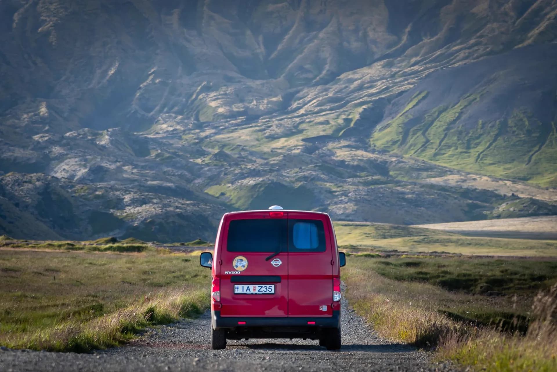 Furgoneta camper roja de KúKú Campers en una pista de grava con montañas de Islandia al fondo
