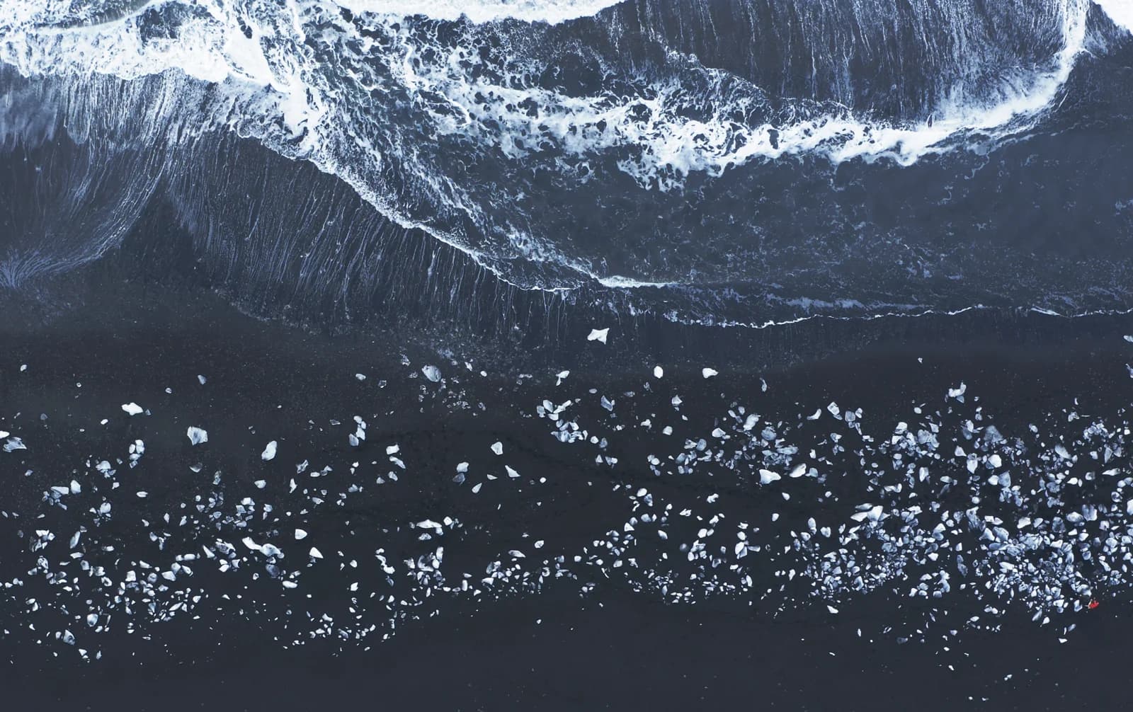 Vista cenital de icebergs esparcidos entre las olas en la arena negra de la Playa de los Diamantes