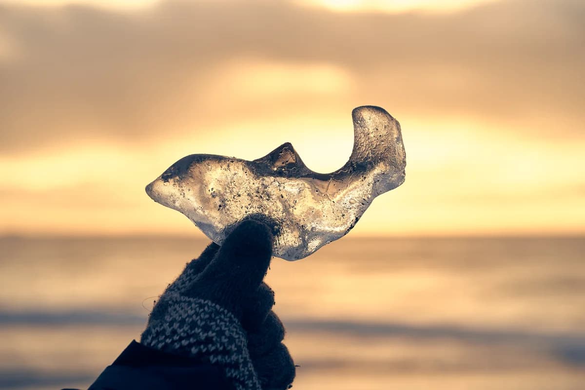 Trozo de hielo con forma de delfín sujeto con la mano al atardecer en la Playa de los Diamantes