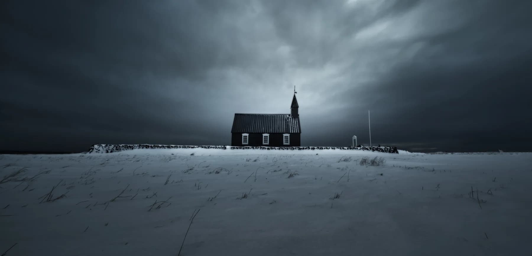 La iglesia negra de Búðakirkja nevada bajo un cielo de tormenta, península de Snæfellsnes