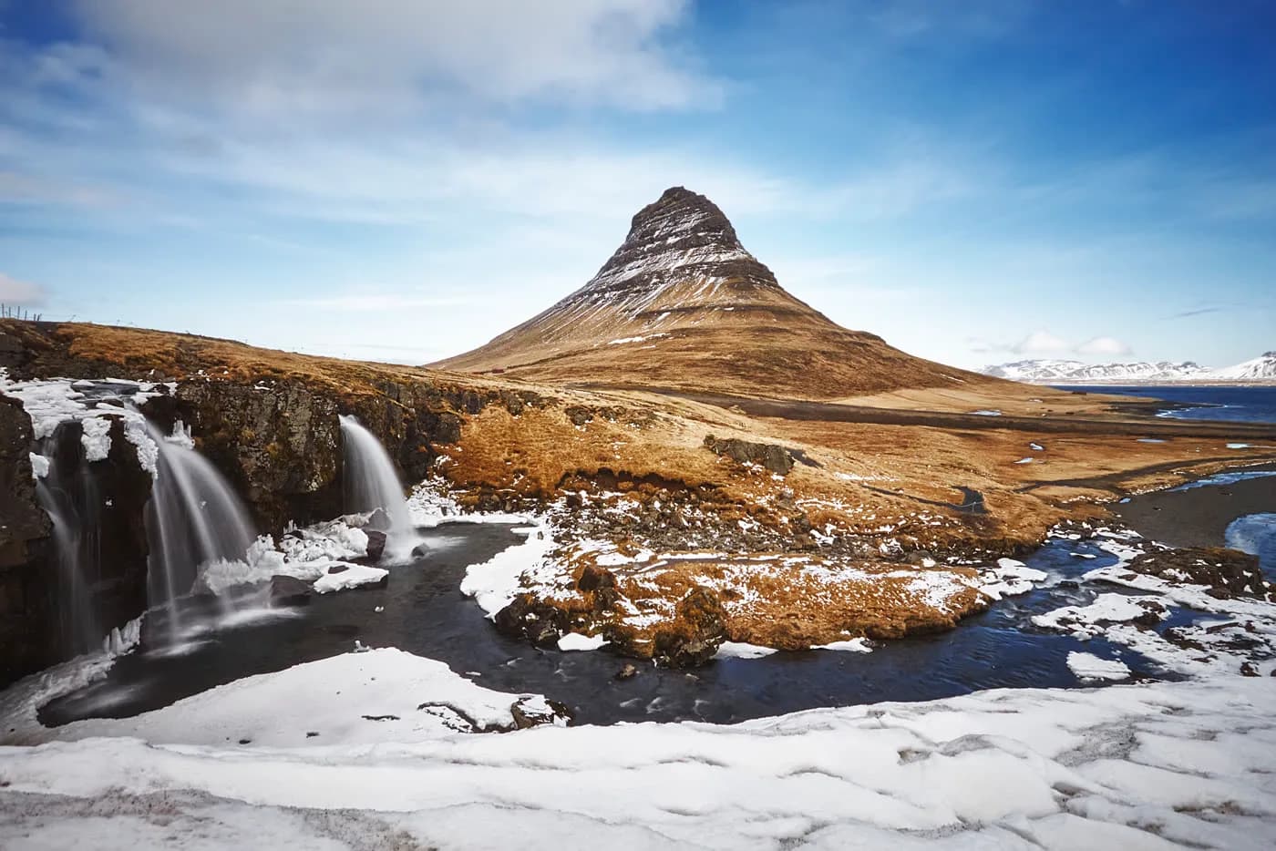 Monte Kirkjufell en primavera con vegetación verde y cielo despejado, Islandia