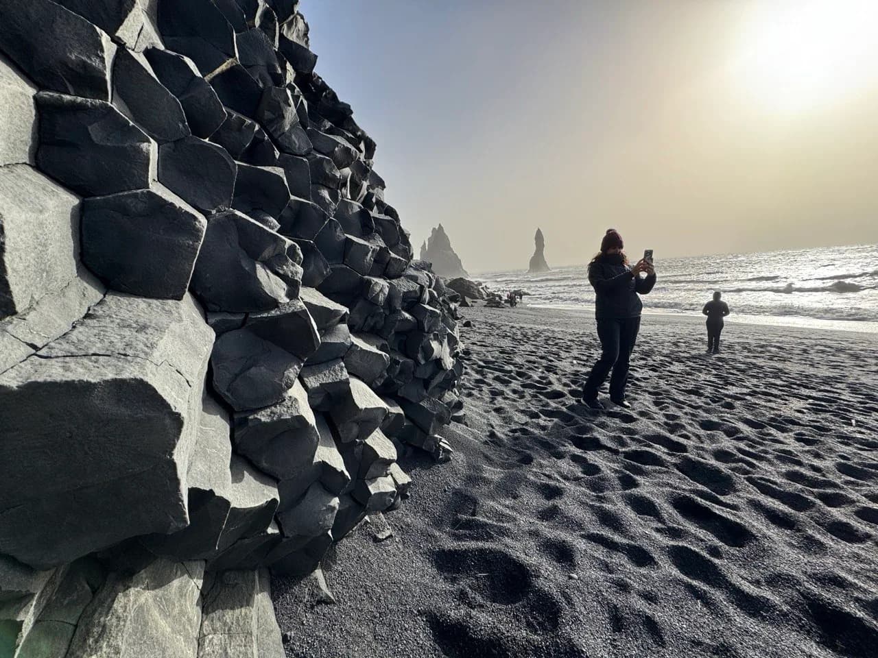 Visitante en la playa negra de Reynisfjara con las columnas de basalto al fondo, sur de Islandia