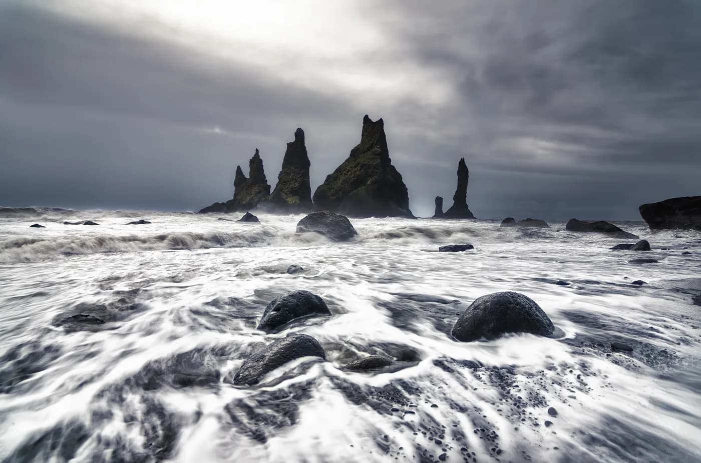 Olas rompiendo con fuerza frente a los Reynisdrangar fotografiados con tele desde la playa negra de Reynisfjara, sur de Islandia
