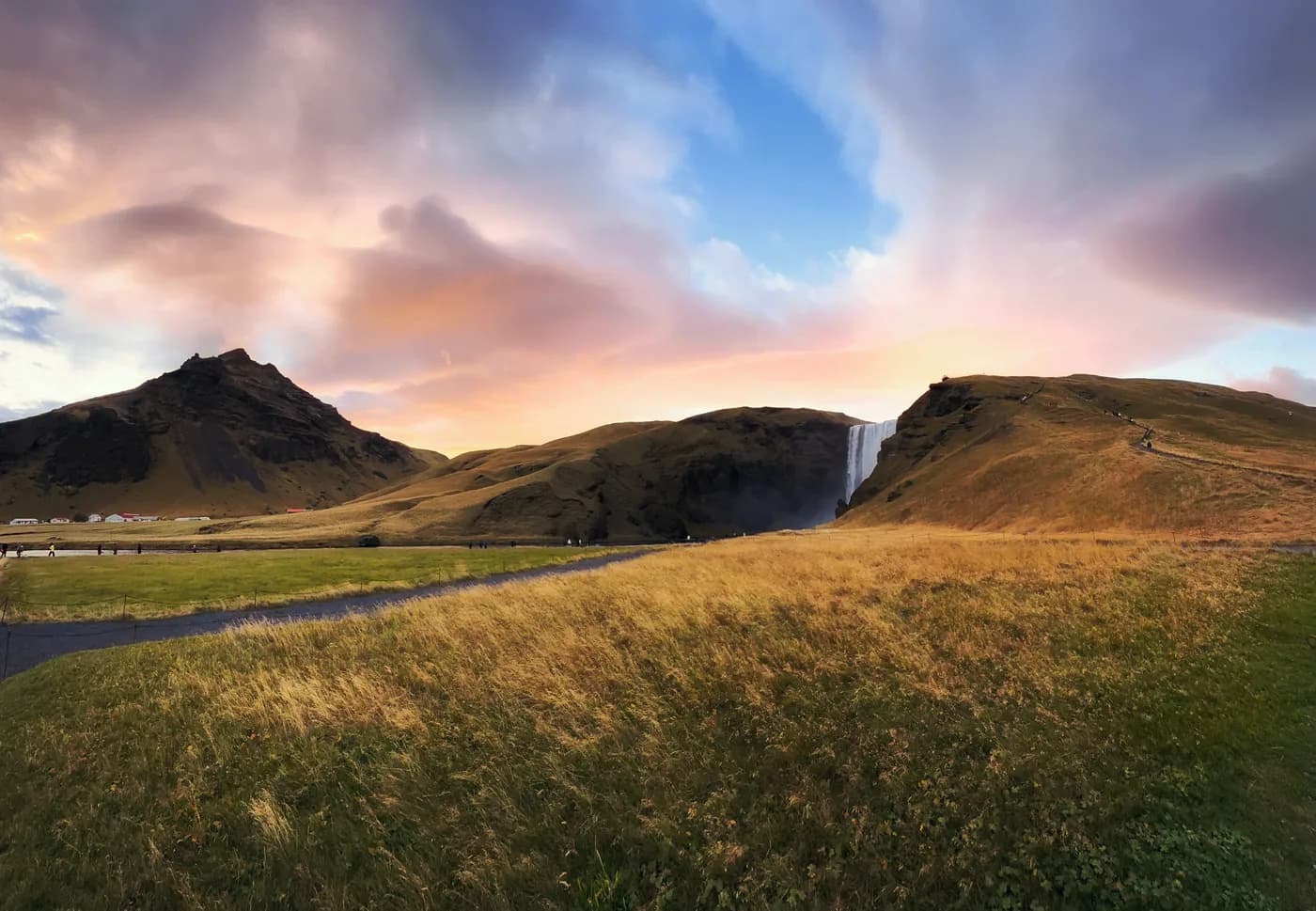 Cascada Skógafoss al amanecer con cielo naranja y dorado, panorámica del sur de Islandia en verano