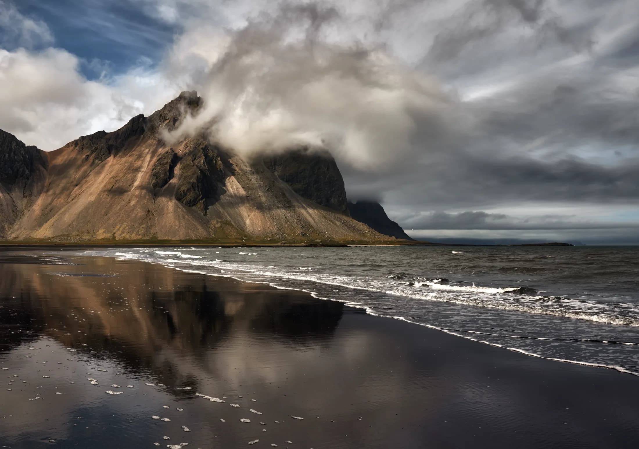 Nubes envolviendo la cima del monte Vestrahorn sobre la playa de arena negra con reflejo, Stokksnes, Islandia