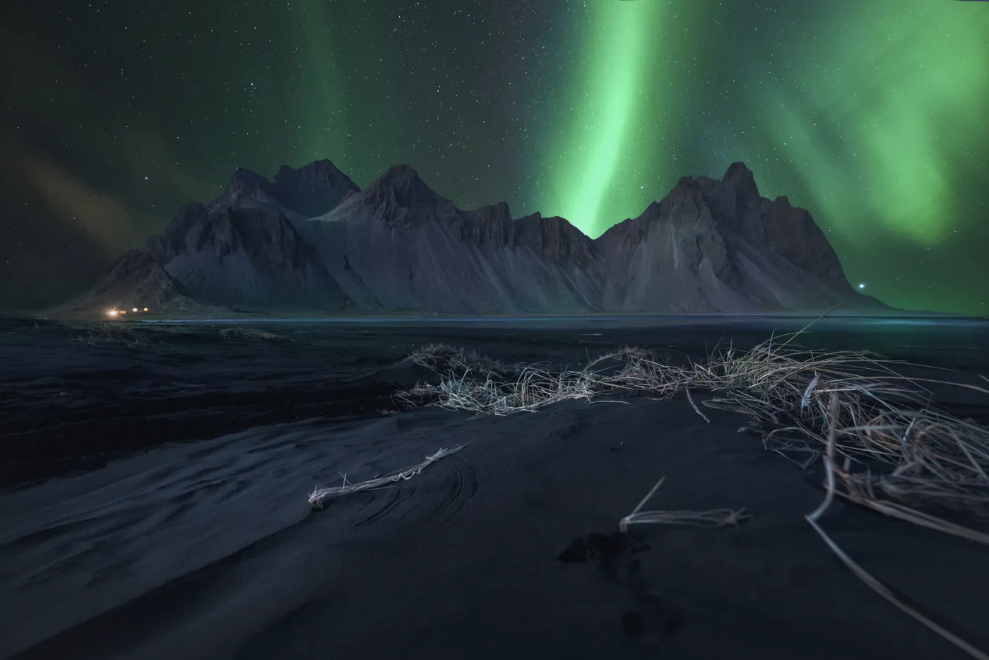 Aurora boreal verde sobre el monte Vestrahorn con hierba seca en primer plano, Stokksnes