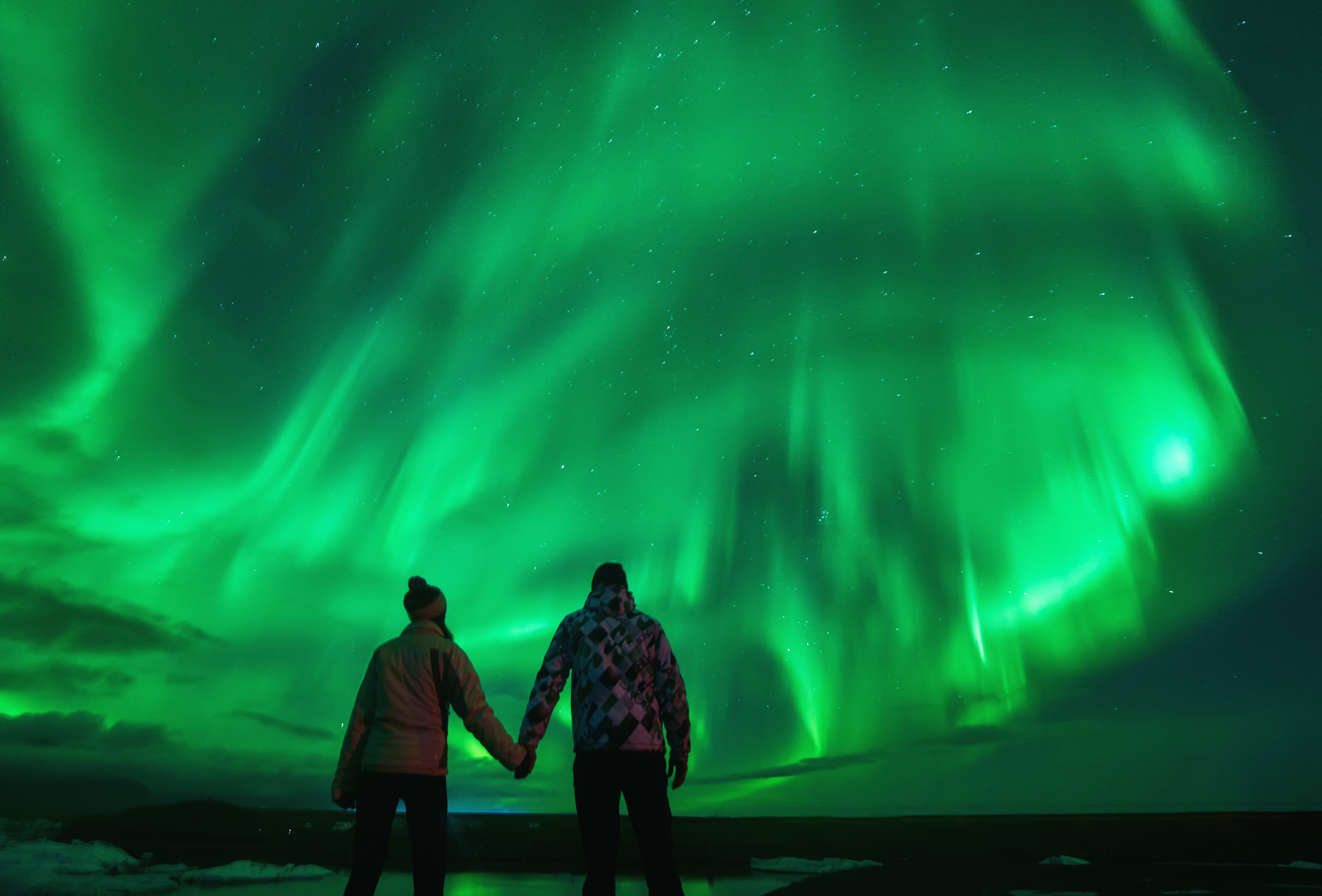 Pareja de viajeros viendo auroras boreales en Jökulsárlón, Islandia — noche de Kp alto con euforia colectiva