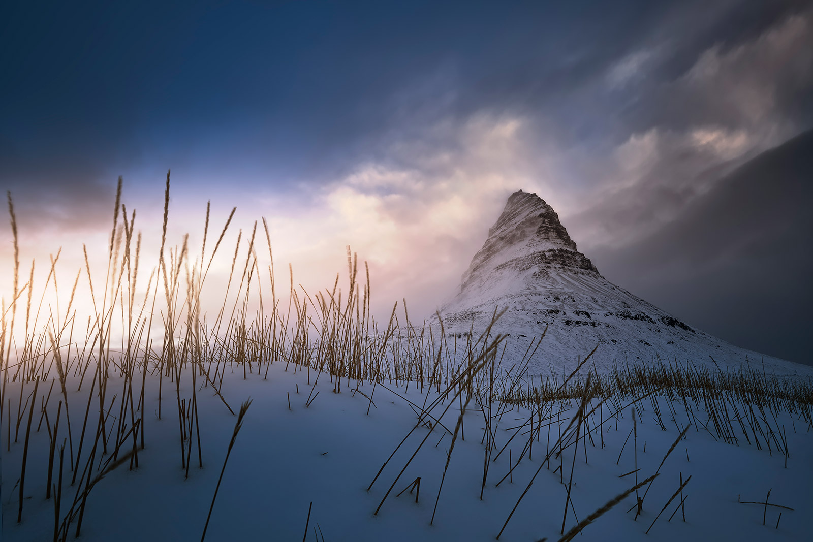 Monte Kirkjufell nevado al amanecer con nubes suaves y una luz cálida iluminando el paisaje.