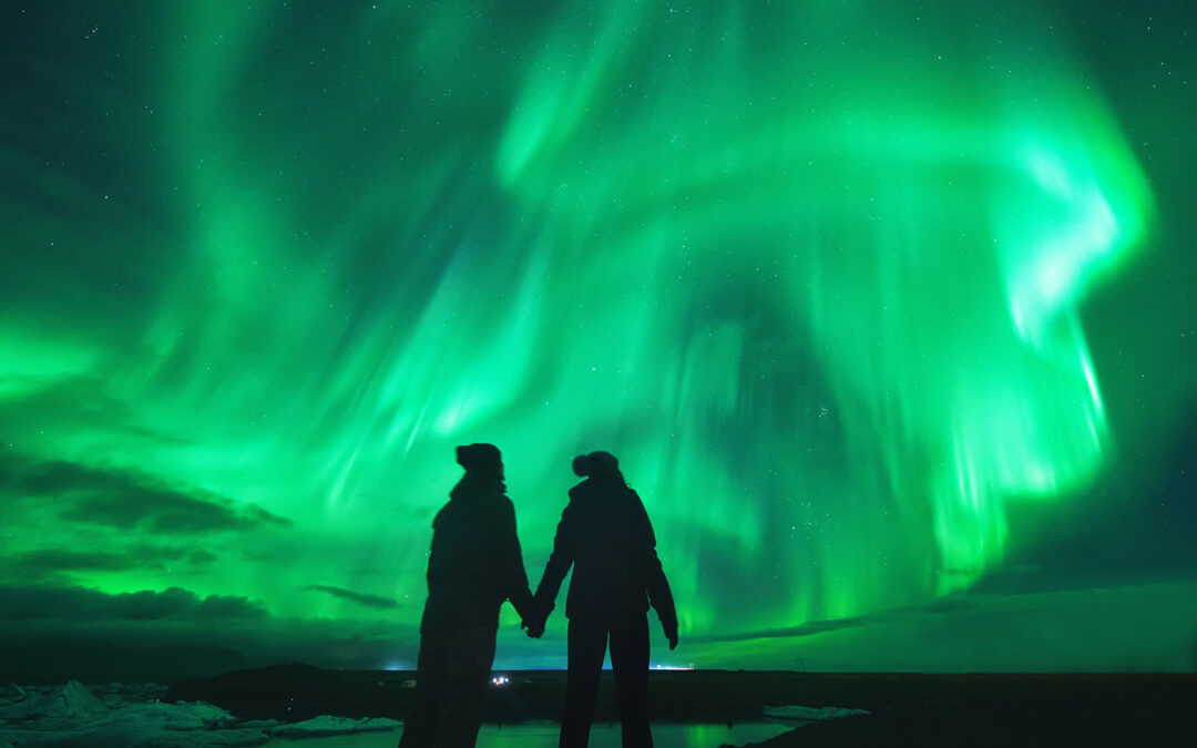 Aurora boreal en Islandia con dos personas a contraluz bajo el cielo iluminado