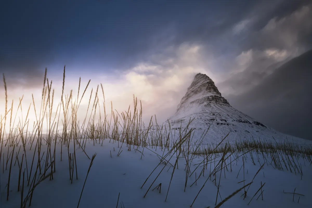 Monte Kirkjufell nevado al amanecer en invierno con luz rosada en el cielo, Islandia