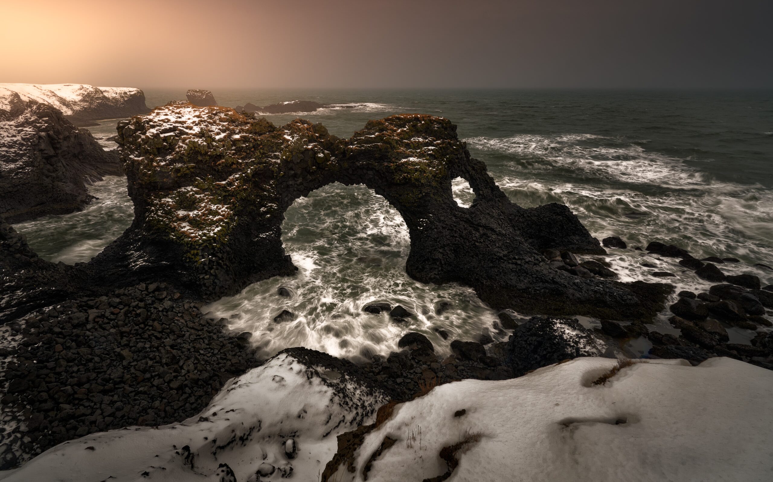 Arco de basalto en Arnarstapi con nieve, Snæfellsnes Arco de basalto en Arnarstapi con olas rompiendo y nieve en primer plano, costa de Snæfellsnes, Islandia