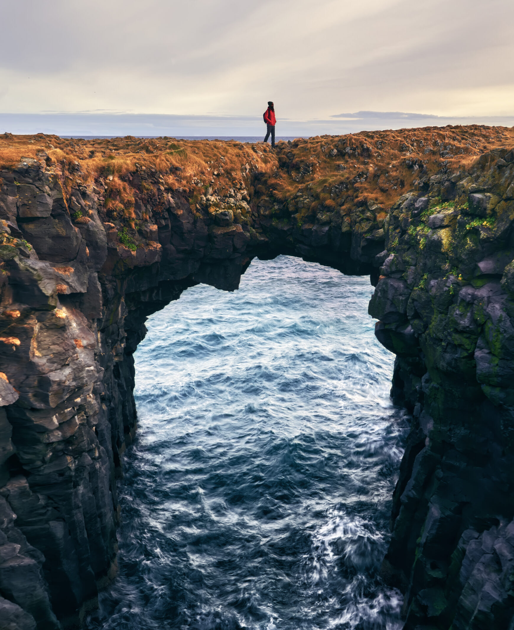Arco de roca en Arnarstapi, Snæfellsnes Arco de roca volcánica en la costa de Arnarstapi con persona en lo alto contemplando el mar, Snæfellsnes, Islandia