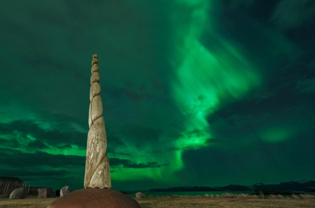 Aurora boreal verde intensa sobre escultura vikinga en el norte de Islandia