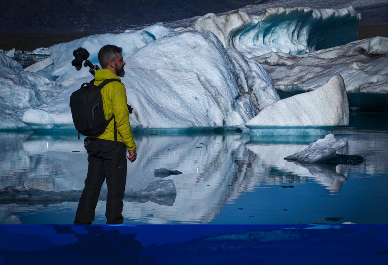 fotografo-jokulsarlon-icebergs-reflejo Fotógrafo con cámara y mochila junto a los icebergs de Jökulsárlón con reflejo azul en el agua