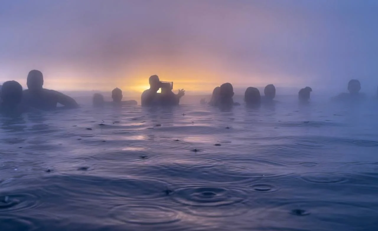 Bañistas disfrutando del atardecer en Sky Lagoon entre vapor de las termas y lluvia suave, Reikiavik