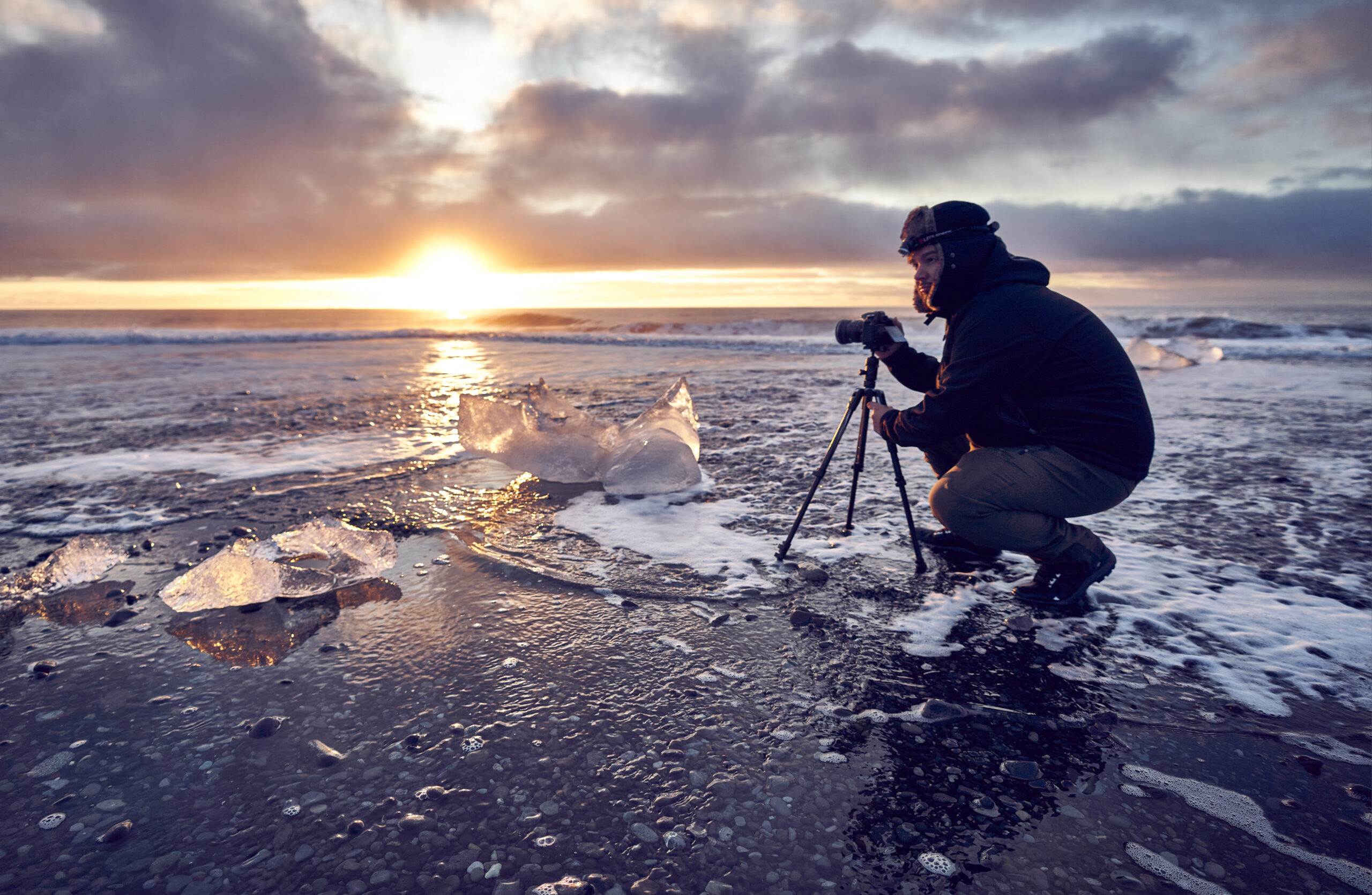 Fotógrafo con trípode haciendo fotografía de larga exposición en la playa de los diamantes de Islandia al amanecer