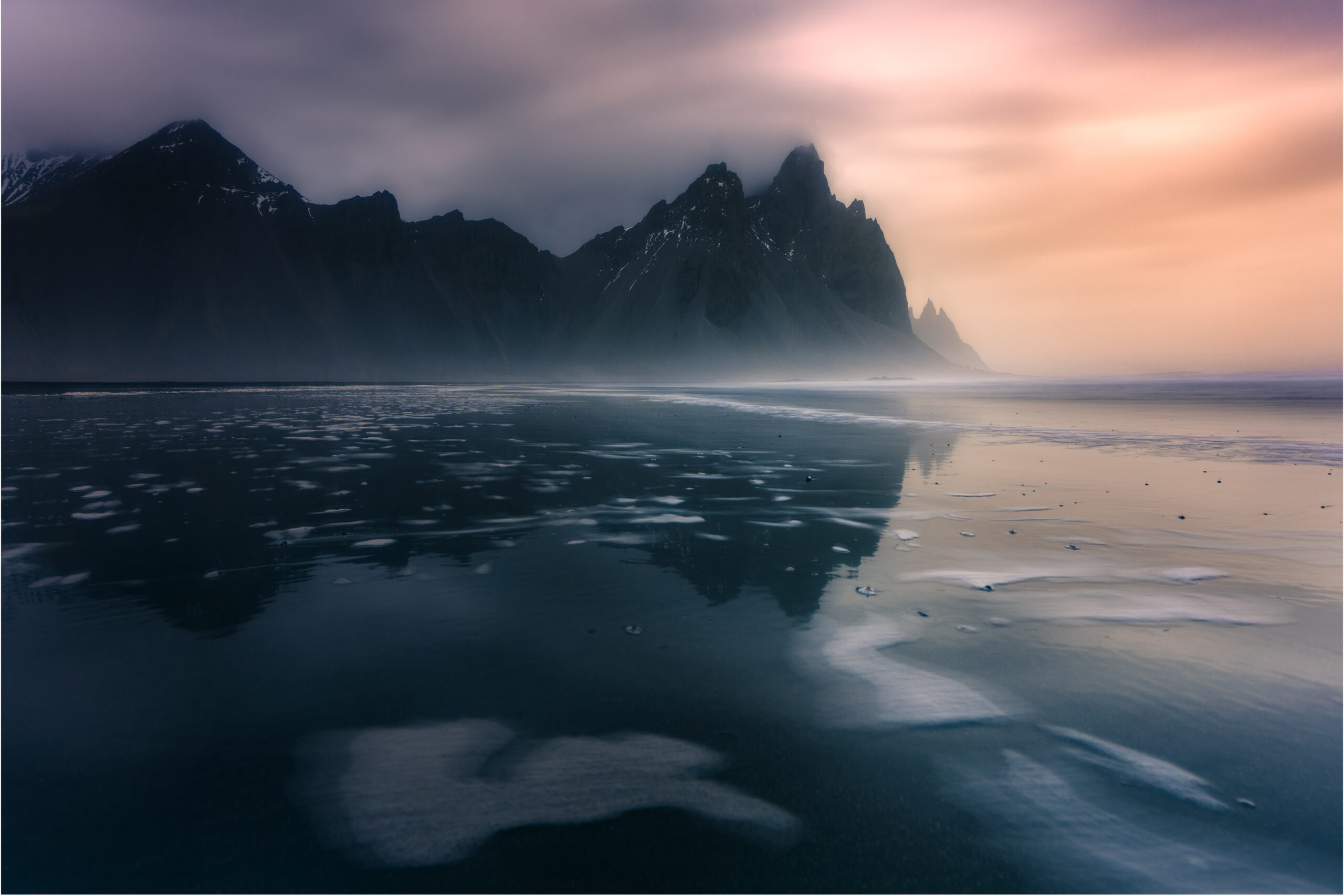 Larga exposición con espuma del mar en Stokksnes y el Vestrahorn entre la niebla Larga exposición con espuma del mar en la playa de Stokksnes y el Vestrahorn al fondo en Islandia